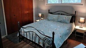 Ein Schlafzimmer mit einem Bett, zwei Nachttischen mit Lampen, einem Deckenventilator, einem Fenster und einer Holztür.