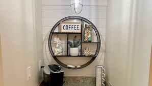 Ein Küchenbereich mit einer Kaffeestation, einem Mülleimer und einem dekorativen Regal mit dem Schriftzug 'COFFEE'.