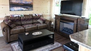 A cozy cabin interior with a wooden interior, a sofa with patterned cushions, a fireplace, and a television. - Cozy Lakefront Cabin on Big Lake, Alaska (Big Lake)