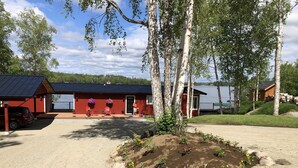 A red building with a black roof, surrounded by trees and a gravel driveway. - Cozy Lakefront Cabin on Big Lake, Alaska (Big Lake)