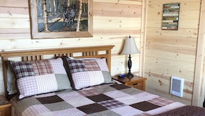 A wooden cabin bedroom with a bed, a nightstand, a lamp, a framed picture, and a cabin rules sign. - Cozy Lakefront Cabin on Big Lake, Alaska (Big Lake)