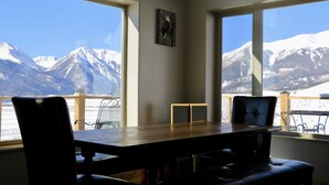 Un comedor con mesa y sillas, ventanas amplias con vista a la montaña y un cuadro pequeño en la pared.