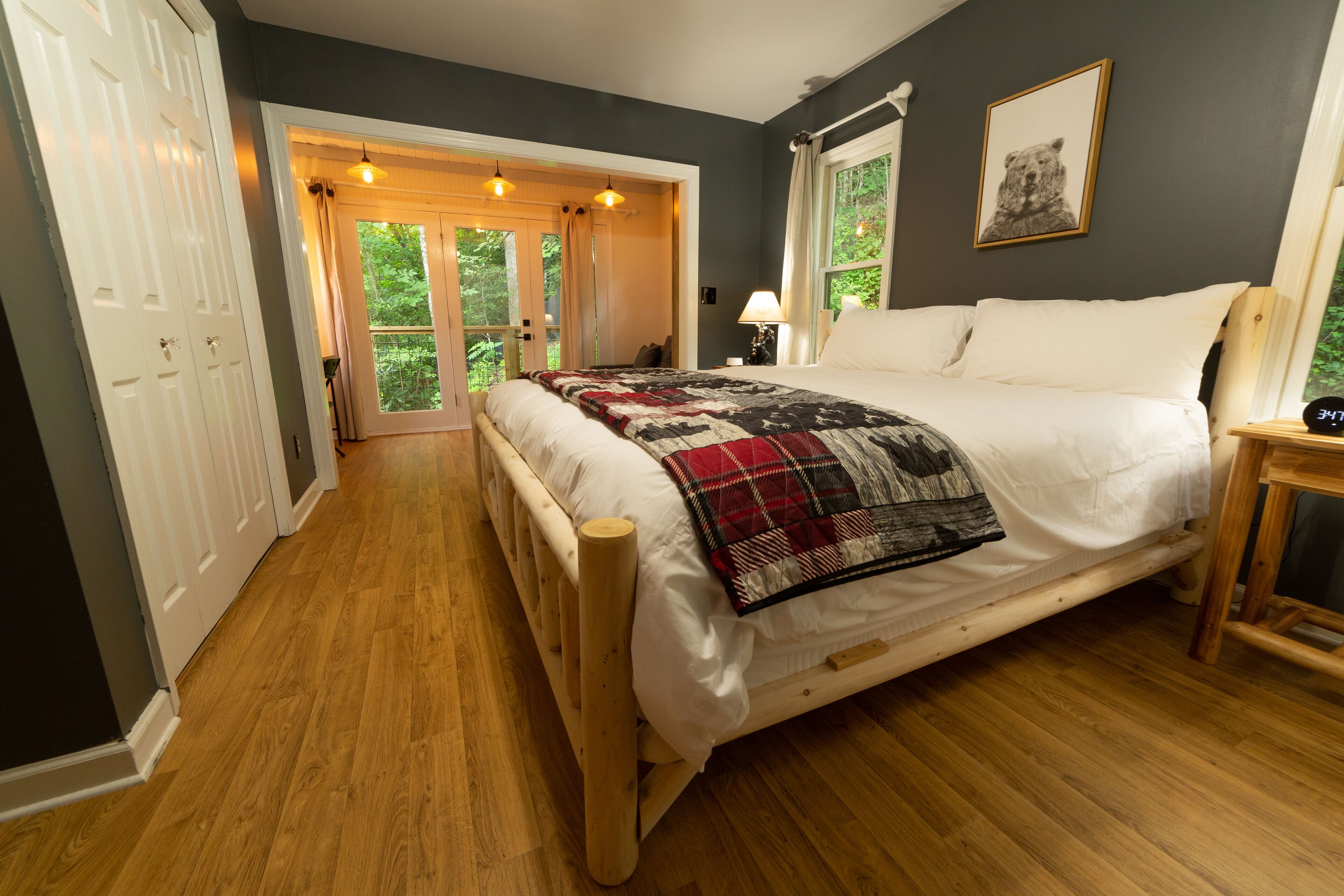 Une chambre à coucher avec un lit en bois, une courtepointe, une table de chevet avec une lampe et une fenêtre décorée d’une image d’ours.
