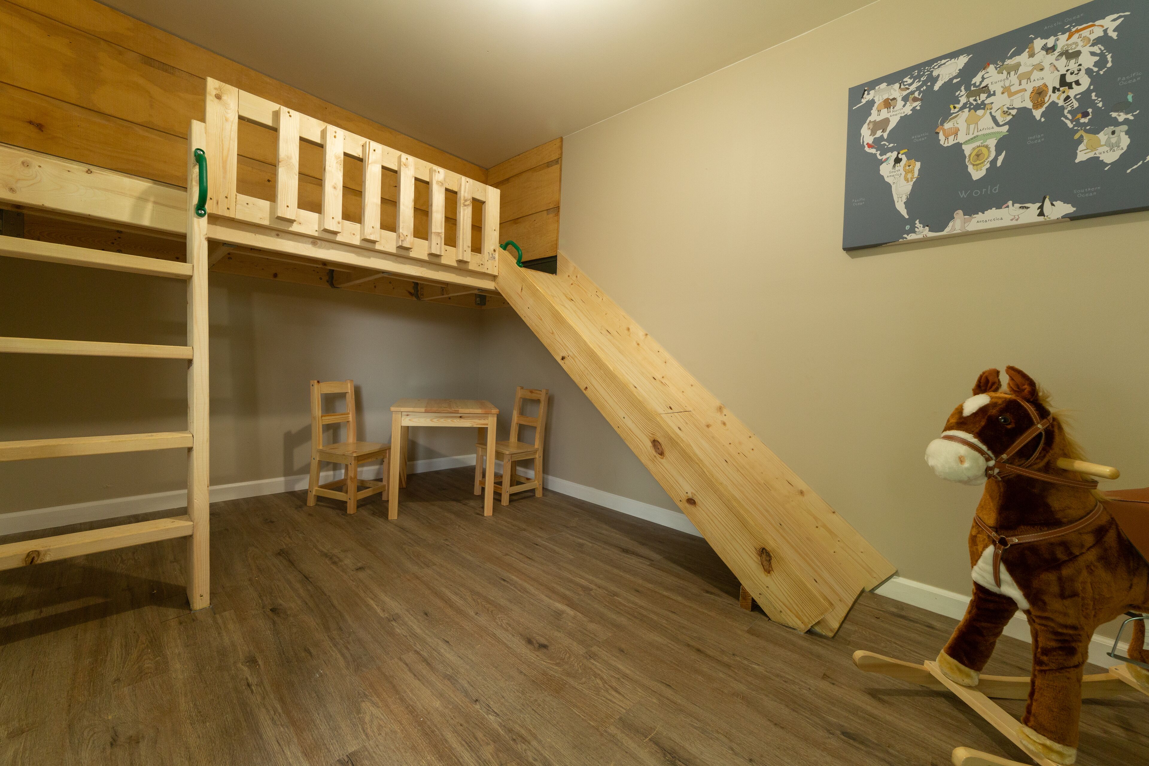Una habitación con una cama litera, un escritorio, dos sillas, un caballito de madera y un mapa mundial en la pared.