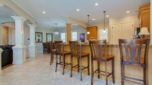 A spacious kitchen with a bar area, wooden chairs, and a large island. - Castle by the Sea 7BR/8BA Luxury Home with Elevator (Hilton Head Island)
