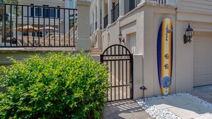 A gated entrance with a gate, a well-maintained hedge, and a surfboard leaning against the building. - Castle by the Sea 7BR/8BA Luxury Home with Elevator (Hilton Head Island)