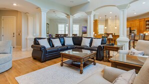 A spacious living room with a sectional sofa, a glass coffee table, and a kitchen area in the background. - Castle by the Sea 7BR/8BA Luxury Home with Elevator (Hilton Head Island)