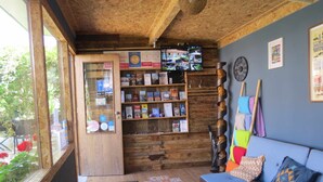 A cozy room with a wooden ceiling, a bookshelf with books and travel brochures, a blue sofa with colorful cushions, and a window with a view of greenery. - Ruby Charm Houses 12 116354/AL (Porto)