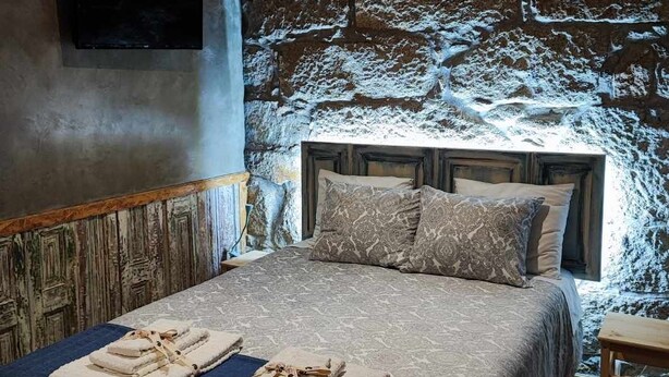A bedroom with a stone wall, a bed with a patterned bedspread, and a flat-screen TV mounted on the wall. - Ruby Charm Houses 12 116354/AL (Porto)