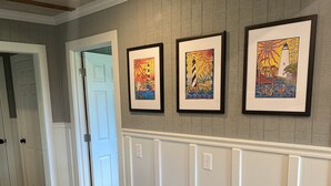A hallway with wooden flooring, white wainscoting, and three framed artworks on the wall. - Our Lucky Charm is a cottage on the waterway in Hatteras Village  (Hatteras)