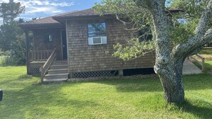 A single-story wooden house with a porch, a small window, and a tree in front. - Our Lucky Charm is a cottage on the waterway in Hatteras Village  (Hatteras)