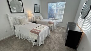 A bedroom with two beds, a nightstand, a dresser, and a window with blinds. - Fabulous 3 Bedroom/ 2 Bath in Alpharetta (Alpharetta)