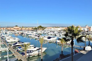 A marina with numerous boats docked, palm trees, and buildings in the background.