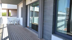 A modern outdoor deck with a table and chairs, large sliding glass doors, and a view of the surrounding area.
