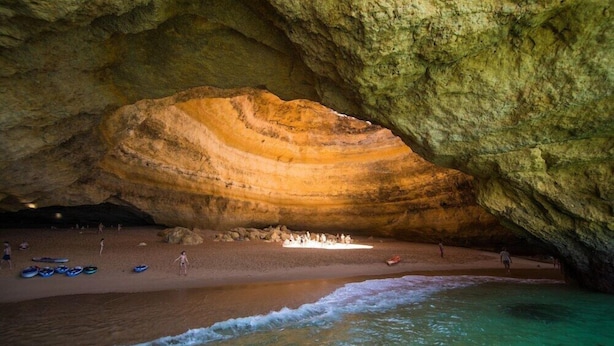 A cave with a large rock formation, a sandy beach, and clear water.