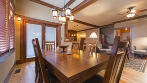A spacious dining area with a wooden table and chairs, a chandelier, and a staircase leading to another level.