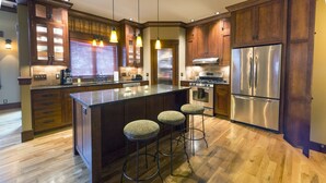 A modern kitchen with wooden cabinets, a stainless steel refrigerator, and a central island with stools.