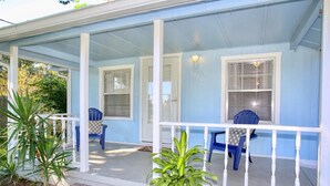 Una casa azul con porche, barandas blancas y dos sillas azules.