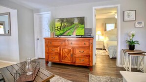 Una sala de estar con un mueble de madera, un televisor, una planta y una cama en la habitación contigua.