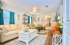 A living room with a beige sofa, a white coffee table, a wooden side table, and a ceiling fan.