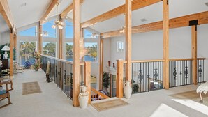 En rummelig indretning med høje lofter, træbjælker, store vinduer og en altan med gelænder.