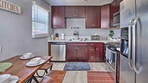 Una cocina compacta con armarios de madera oscura, electrodomésticos de acero inoxidable y un comedor con mesa y bancos de madera.