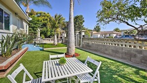 Un patio exterior bien cuidado con una mesa y sillas blancas, rodeado de abundante vegetación y una palmera.
