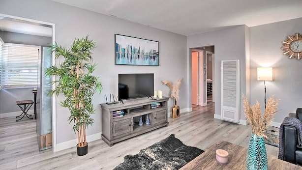 Una sala de estar moderna con un televisor de pantalla plana, una planta grande en maceta, una mesa de centro de madera y un tapete negro.