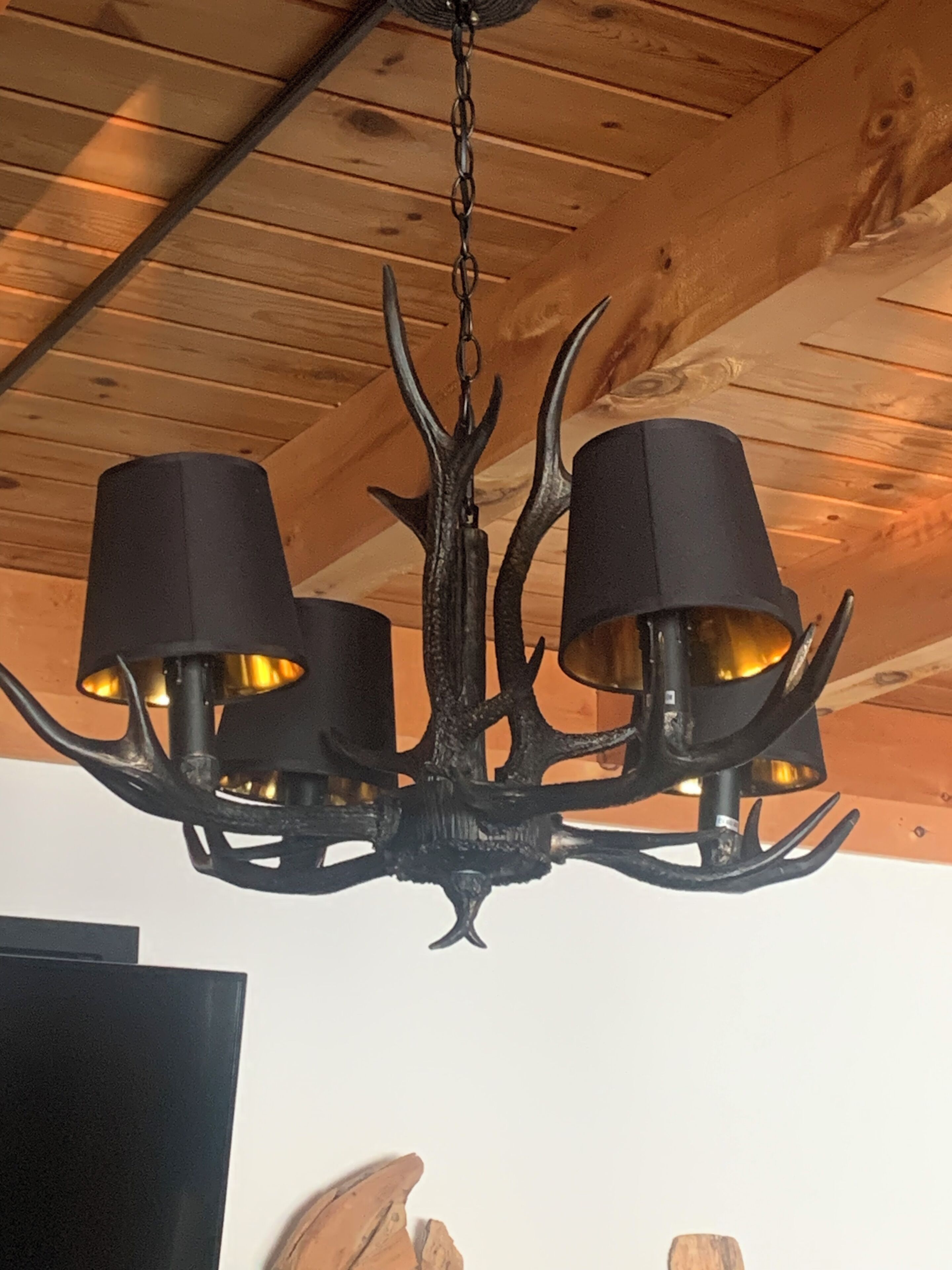 A chandelier with a black finish and three lampshades, hanging from a wooden ceiling.