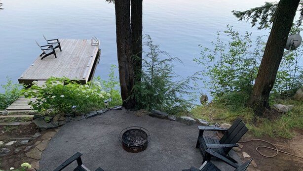 A circular seating area with a fire pit surrounded by chairs, overlooking a body of water. - Muskoka Waterfront Retreat (Port Carling)