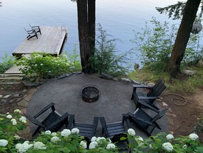 A circular seating area with a fire pit surrounded by chairs, overlooking a body of water. - Muskoka Waterfront Retreat (Port Carling)