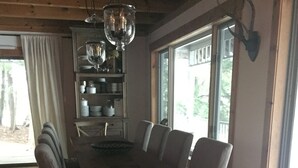 A dining area with a wooden table and chairs, a chandelier, and a large window with a view of trees. - Muskoka Waterfront Retreat (Port Carling)