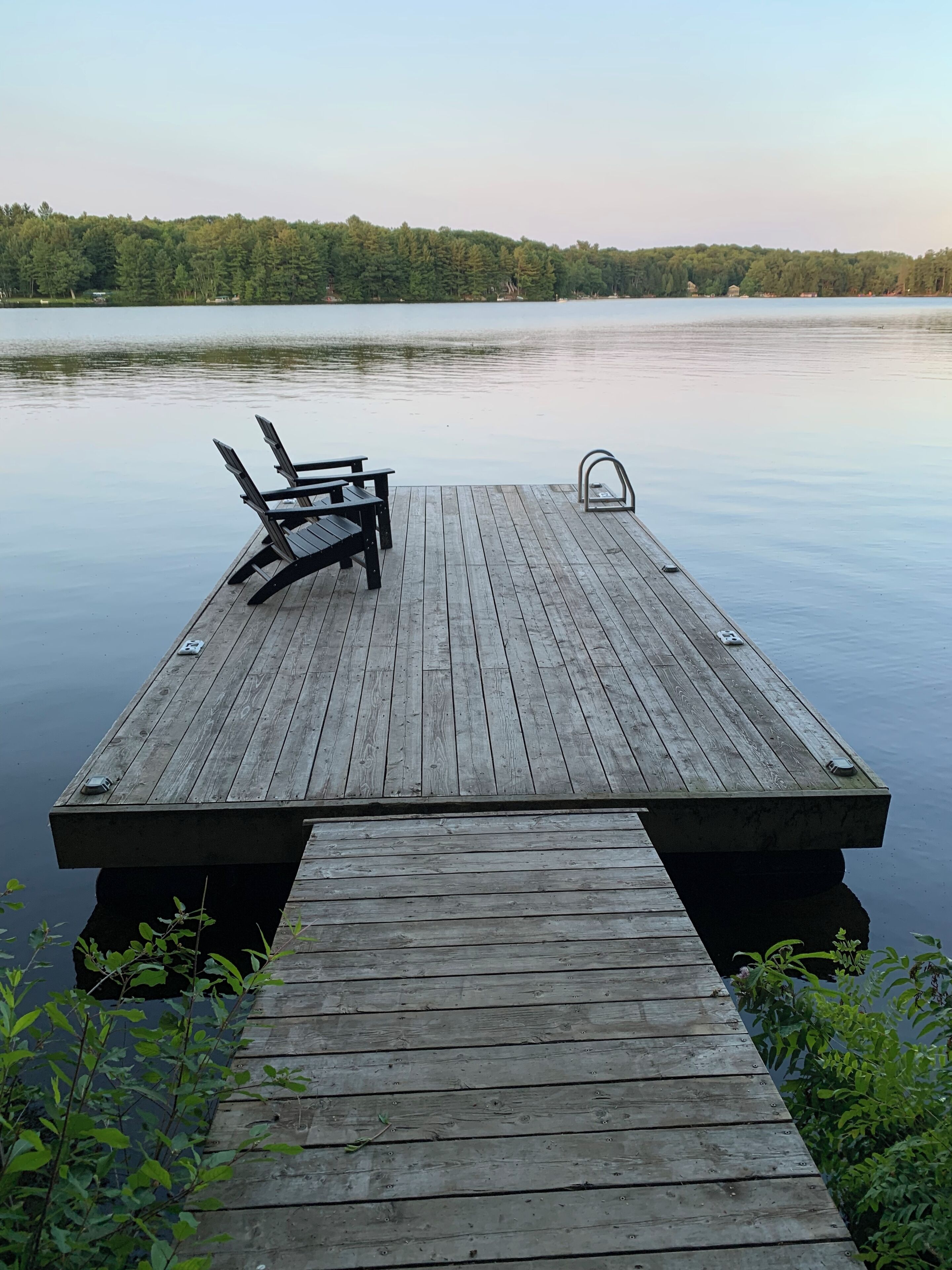 A wooden dock extending into calm water with a bench and a metal railing.