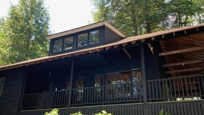 A cabin with a covered porch, wooden deck, and a garden with various plants and a chair. - Muskoka Waterfront Retreat (Port Carling)