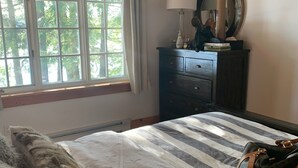 A bedroom with a large bed, a dresser with a mirror, and a window with curtains. - Muskoka Waterfront Retreat (Port Carling)