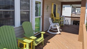 A covered porch with green Adirondack chairs, a wooden table, and a rocking chair. - West Side Near Avalon Pier ~ Hot Tub~Dog Friendly~Firepit + Fenced in Yard (Kill Devil Hills)
