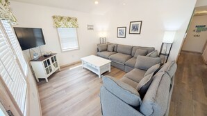 A living room with a sofa, a coffee table, a TV, and a cabinet. - West Side Near Avalon Pier ~ Hot Tub~Dog Friendly~Firepit + Fenced in Yard (Kill Devil Hills)