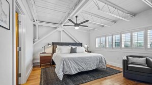A bedroom with a bed, a nightstand, a desk, a chair, a ceiling fan, and large windows. - Hogs Hideaway On Dickson St. (Fayetteville)