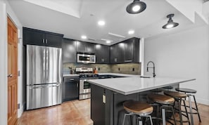 A modern kitchen with stainless steel appliances, dark cabinetry, and a central island with stools. - Hogs Hideaway On Dickson St. (Fayetteville)