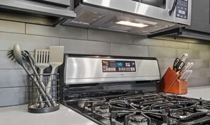 A kitchen with a stainless steel stove, a digital clock, and utensils in holders.