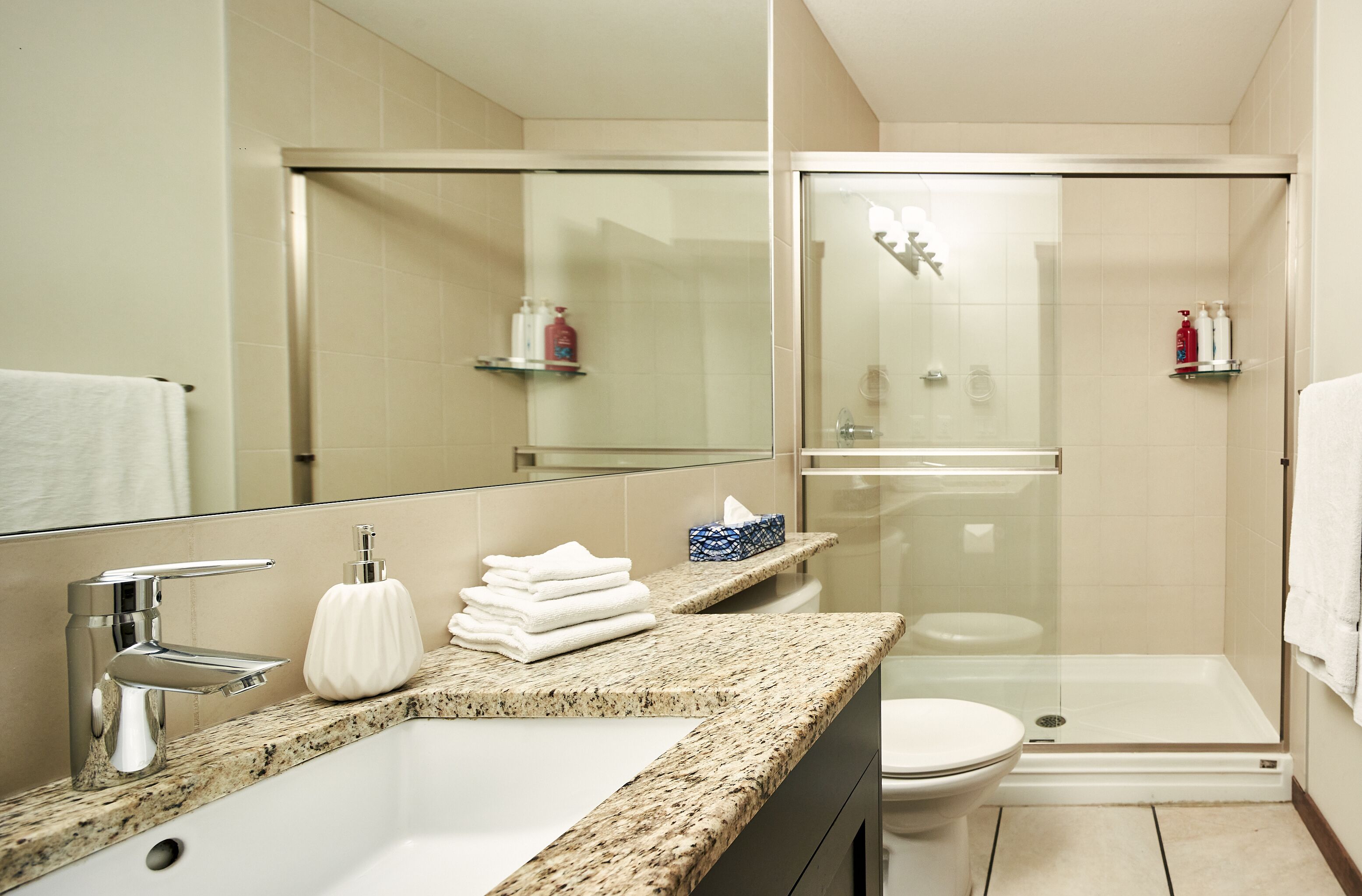 A modern bathroom with a granite countertop, a white sink, a toilet, and a glass-enclosed shower area.