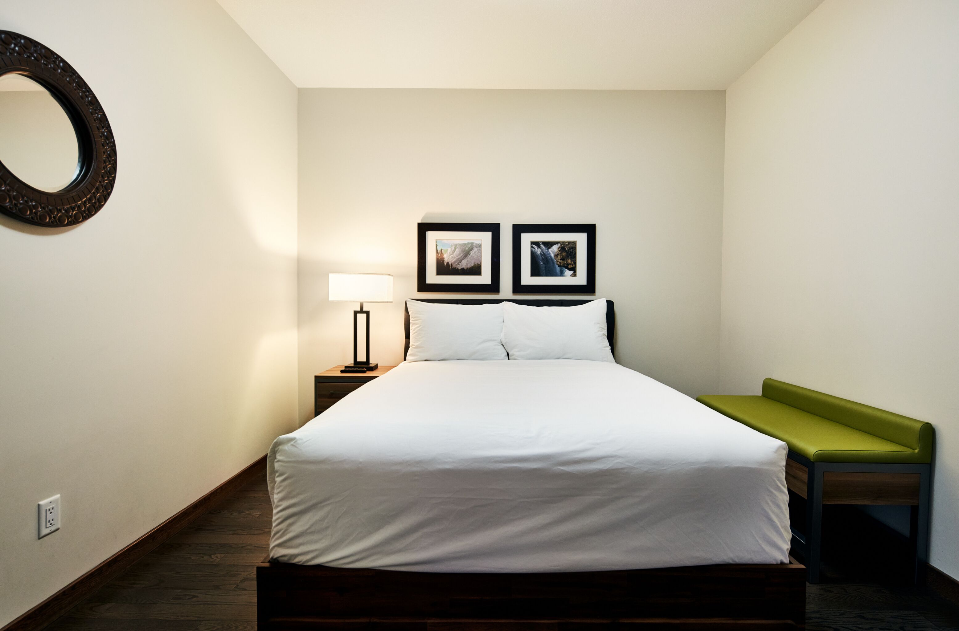 Een keurig opgemaakte slaapkamer met een bed, nachtkastje, lamp en twee ingelijste foto's aan de muur.