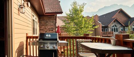 A wooden deck with a barbecue grill, a table, and chairs.