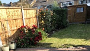 A paved patio area with a wooden fence, potted plants, and a grassy lawn.