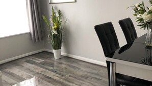 A modern dining area with a glass table, black upholstered chairs, a potted plant, and a large window with curtains.