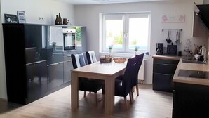 A modern kitchen with a dining table, chairs, a refrigerator, and a coffee machine. - Ferienwohnung Rieslingfreude - Erleben Sie Freude bei Freunden! (Rüdesheim am Rhein)