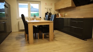 A modern kitchen with wooden cabinets, a dining table with chairs, and a large window providing a view of the outdoors. - Ferienwohnung Rieslingfreude - Erleben Sie Freude bei Freunden! (Rüdesheim am Rhein)