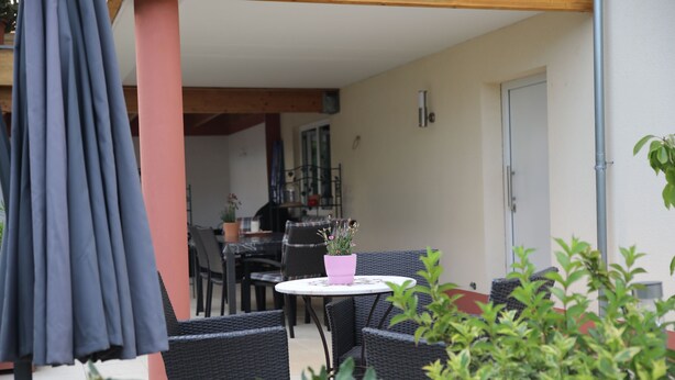 An outdoor patio area with wicker furniture, a round table with a pink flower pot, and a blue umbrella. - Ferienwohnung Rieslingfreude - Erleben Sie Freude bei Freunden! (Rüdesheim am Rhein)