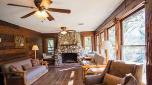 A cozy living room with a stone fireplace, wooden furniture, and large windows. - Sierra Sky Ranch (Oakhurst)