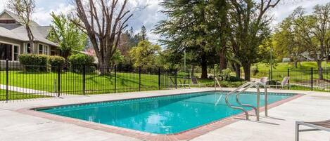 A rectangular swimming pool with a metal ladder, surrounded by a concrete deck and a black metal fence.